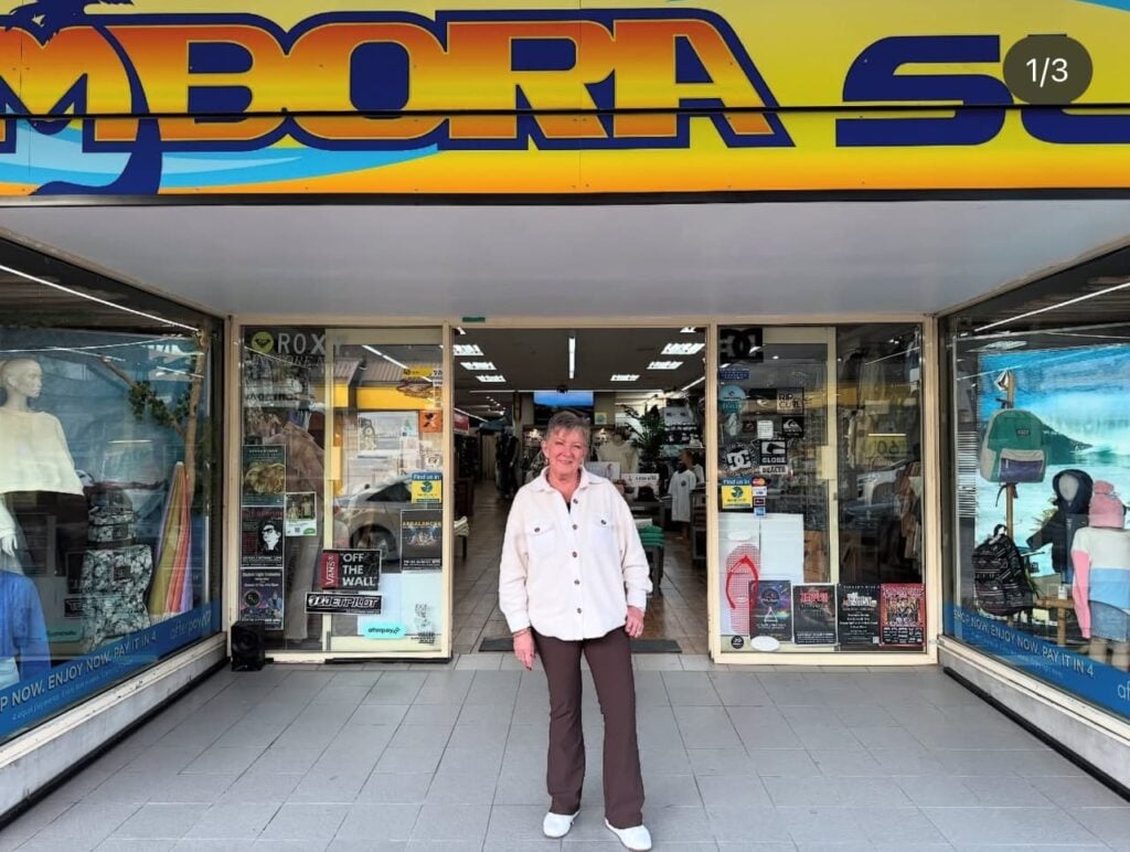 A older woman is standing directly in front of the entrance of a retail store.