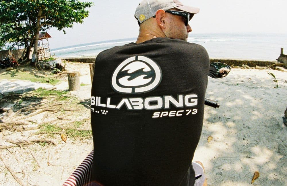 A man is photographed from behind while sitting on a motorbike or scooter, looking towards the ocean.